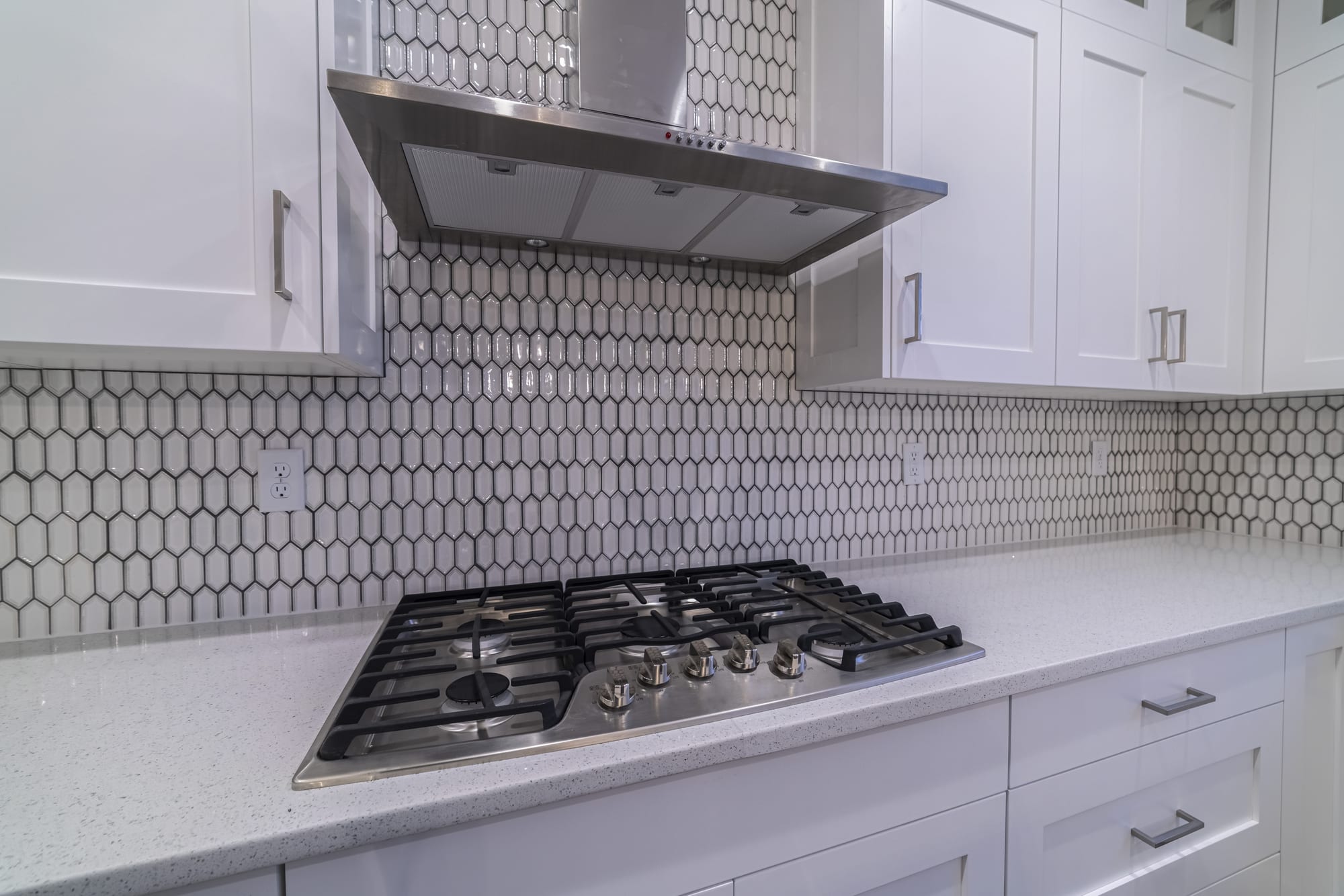 Modern gas cooker hob and extractor fan in a fitted white kitchen with honeycomb splash back